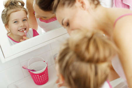 Mother and her daughter brush their teeth with toothbrushes in the bathroom at home. Mom and baby girl in home clothes. High quality photo.の写真素材