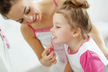 Mother and her daughter brush their teeth with toothbrushes in the bathroom at home. Mom and baby girl in home clothes. High quality photo.の写真素材