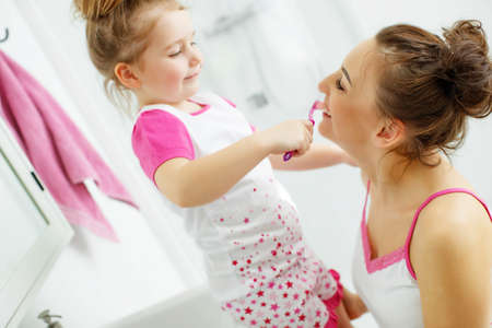 Mother and her daughter brush their teeth with toothbrushes in the bathroom at home. Mom and baby girl in home clothes. High quality photo.の写真素材