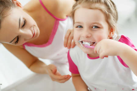 Mother and her daughter brush their teeth with toothbrushes in the bathroom at home. Mom and baby girl in home clothes. High quality photo.の写真素材