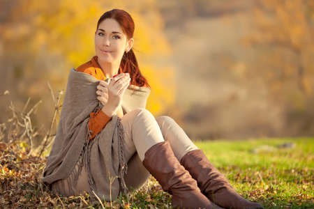 A woman in warm knitted clothes drinks a cup of hot tea or coffee outdoors in the sunlight. High quality photo.の写真素材