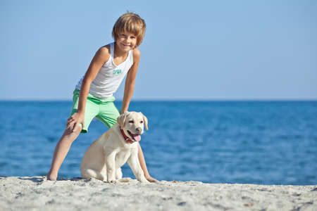 Happy boy playing with his dog on the seashore against the blue sky. Best friends have fun on vacation. High quality photo.の写真素材