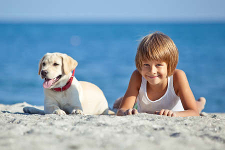 Happy boy playing with his dog on the seashore against the blue sky. Best friends have fun on vacation. High quality photo.の写真素材