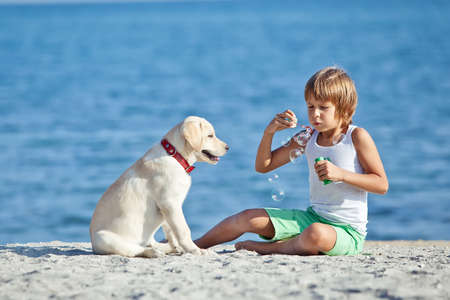 Happy boy playing with his dog on the seashore against the blue sky. Best friends have fun on vacation. High quality photo.の写真素材