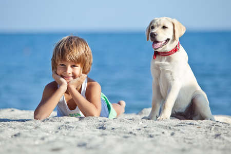 Happy boy playing with his dog on the seashore against the blue sky. Best friends have fun on vacation. High quality photo.の写真素材