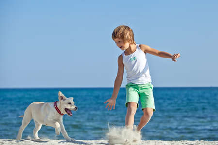 Happy boy playing with his dog on the seashore against the blue sky. Best friends have fun on vacation. High quality photo.の写真素材