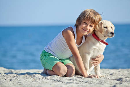Happy boy playing with his dog on the seashore against the blue sky. Best friends have fun on vacation. High quality photo.の写真素材