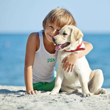 Happy boy playing with his dog on the seashore against the blue sky. Best friends have fun on vacation, play on the sand against the sea. High quality photo.の写真素材