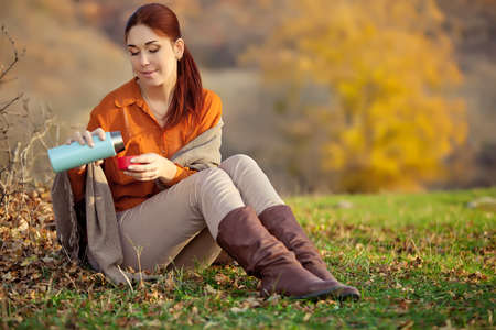 A woman in warm knitted clothes drinks a cup of hot tea or coffee outdoors in the sunlight. High quality photo.の写真素材