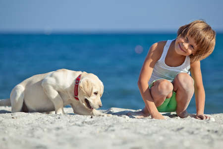 Happy boy playing with his dog on the seashore against the blue sky. Best friends have fun on vacation, play on the sand against the sea. High quality photo.の写真素材