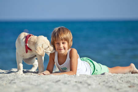 Happy boy playing with his dog on the seashore against the blue sky. Best friends have fun on vacation, play on the sand against the sea. High quality photo.の写真素材