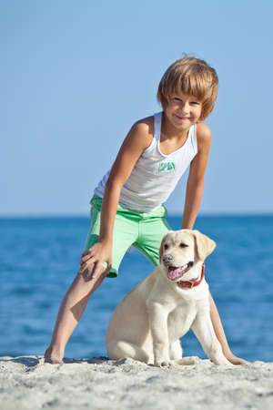 Happy boy playing with his dog on the seashore against the blue sky. Best friends have fun on vacation, play on the sand against the sea. High quality photo.の写真素材