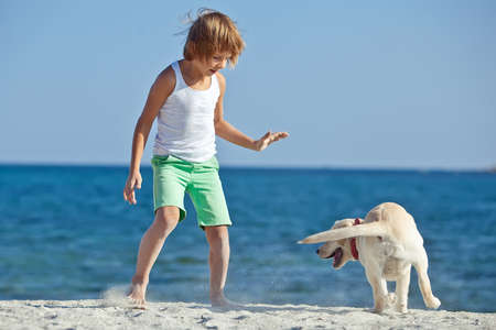 Happy boy playing with his dog on the seashore against the blue sky. Best friends have fun on vacation, play on the sand against the sea. High quality photo.の写真素材