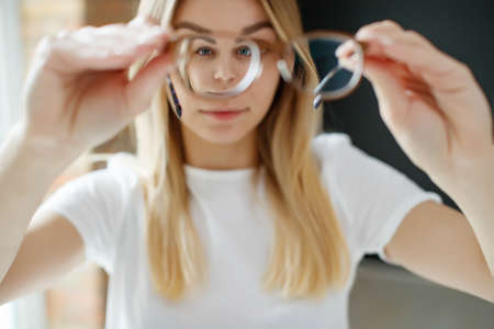 A woman has vision problems, squints when trying to see something, takes off her glasses, is isolated. Myopia, hyperopia, vision concept. High quality photo.の写真素材