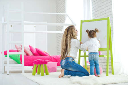 Happy loving family. Mother and daughter in the childrens room. Funny mom and lovely baby having fun indoors. Cute little girl is playing with a woman. High quality photo.の写真素材