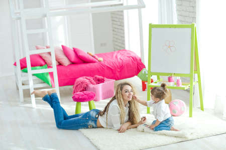 Happy loving family. Mother and daughter in the childrens room. Funny mom and lovely baby having fun indoors. Cute little girl is playing with a woman. High quality photo.の写真素材