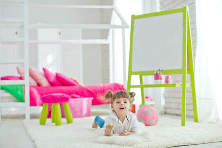 Cute little baby girl on the carpet at home. Funny lovely baby having fun in the nursery. High quality photo.の写真素材