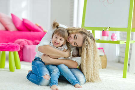 Happy loving family. Mother and daughter in the childrens room. Funny mom and lovely baby having fun indoors. Cute little girl is playing with a woman. High quality photo.の写真素材
