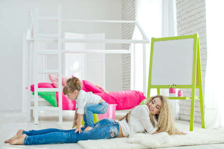 Happy loving family. Mother and daughter in the childrens room. Funny mom and lovely baby having fun indoors. Cute little girl is playing with a woman. High quality photo.の写真素材