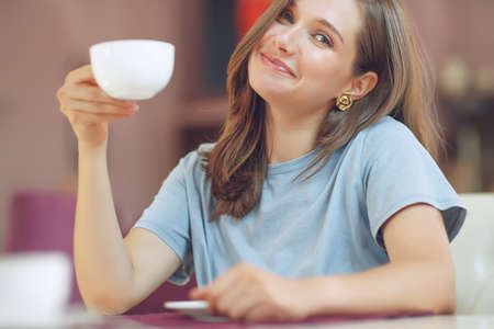 Thoughtful mature woman sits in a cafeteria holding a coffee mug. A middle-aged woman drinks tea while thinking. Relaxing and thinking while drinking coffee. High quality photo.の写真素材