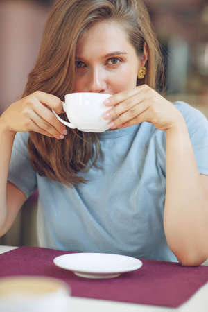 Thoughtful mature woman sits in a cafeteria holding a coffee mug. A middle-aged woman drinks tea while thinking. Relaxing and thinking while drinking coffee. High quality photo.の写真素材