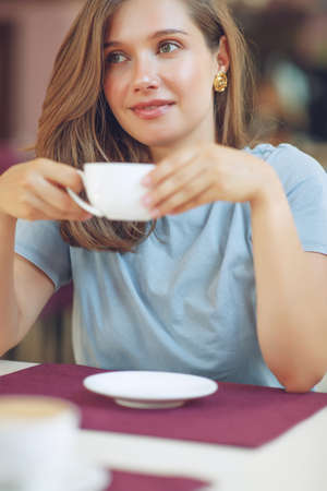 Thoughtful mature woman sits in a cafeteria holding a coffee mug. A middle-aged woman drinks tea while thinking. Relaxing and thinking while drinking coffee. High quality photo.の写真素材
