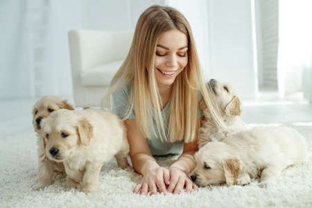 Cute young woman kisses and hugs a Labrador Retriever puppy dog. Love between owner and dog. In the room at home, interior. High quality photo.の写真素材