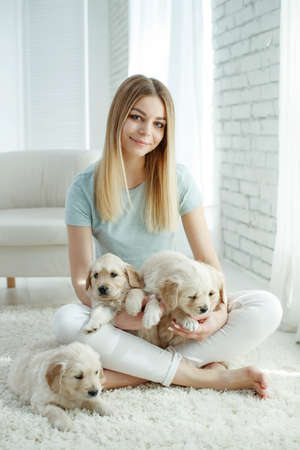 Cute young woman kisses and hugs a Labrador Retriever puppy dog. Love between owner and dog. In the room at home, interior. High quality photo.の写真素材