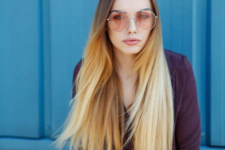 Close up shot of stylish young woman in sunglasses smiling against blue background. Beautiful female model with copy space. High quality photo.の写真素材