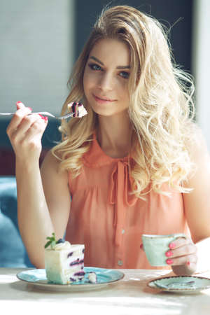 Young beautiful woman eating dessert. Cheerful attractive young woman with long hair and eating dessert. High quality photo.の写真素材