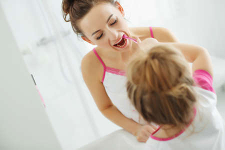 Mother and her daughter brush their teeth with toothbrushes in the bathroom at home. Mom and baby girl in home clothes. High quality photo.の写真素材