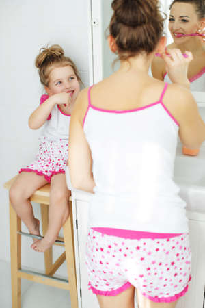 Mother and her daughter brush their teeth with toothbrushes in the bathroom at home. Mom and baby girl in home clothes. High quality photo.の写真素材