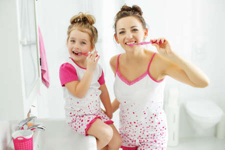 Mother and her daughter brush their teeth with toothbrushes in the bathroom at home. Mom and baby girl in home clothes. High quality photo.の写真素材