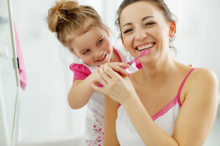 Mother and her daughter brush their teeth with toothbrushes in the bathroom at home. Mom and baby girl in home clothes. High quality photo.の写真素材