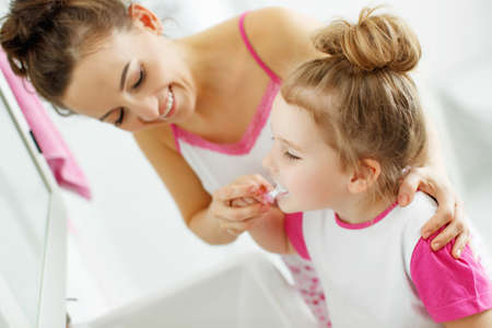 Mother and her daughter brush their teeth with toothbrushes in the bathroom at home. Mom and baby girl in home clothes. High quality photo.の写真素材