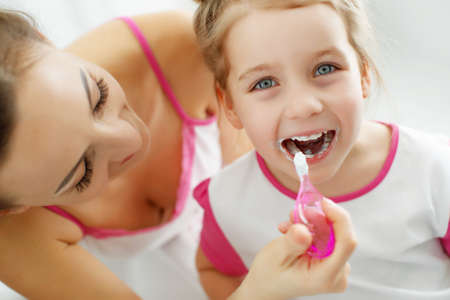 Mother and her daughter brush their teeth with toothbrushes in the bathroom at home. Mom and baby girl in home clothes. High quality photo.の写真素材