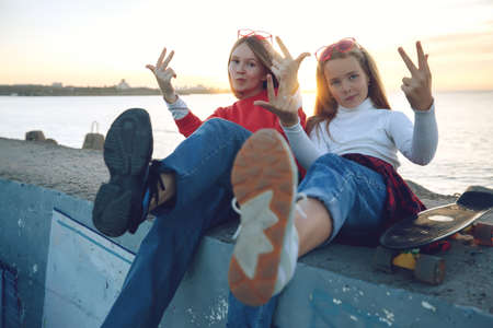Two female friends playing with skateboard skateboard in the park. Girls with a skateboard. Laughter and fun. High quality photo.の写真素材