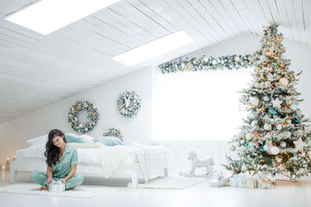 Beautiful woman, warm and cozy day in Christmas interior design, Christmas tree decorated. High quality photo.の写真素材