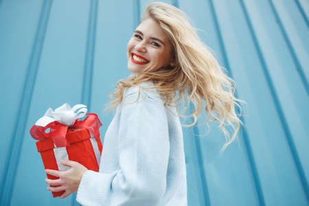 Happy woman in a gift box and looking at the camera, on a blue background. High quality photo.の写真素材