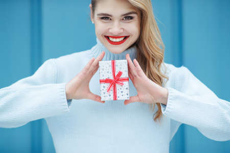 Happy pretty young woman holding a gift box over blue background. High quality photo.の写真素材