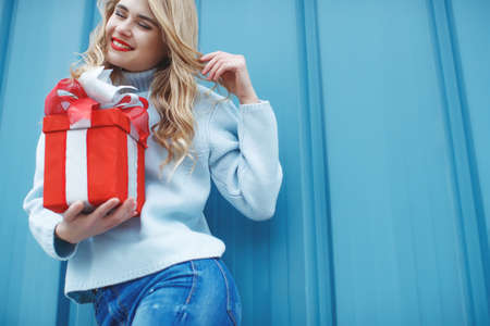 Happy pretty young woman holding a gift box over blue background. High quality photo.の写真素材