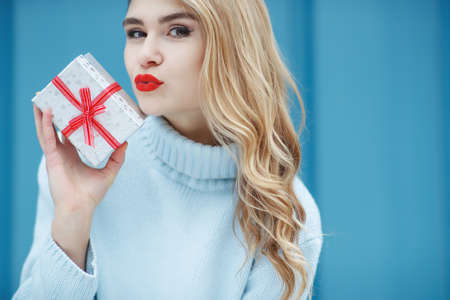 Happy pretty young woman holding a gift box over blue background. High quality photo.の写真素材