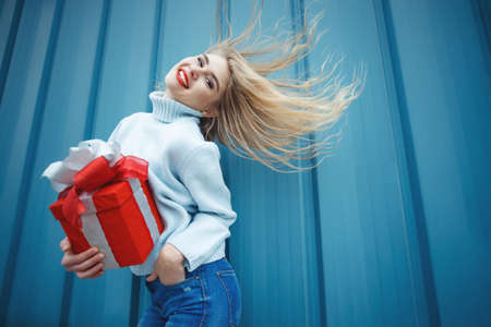 Happy pretty young woman holding a gift box over blue background. High quality photo.の写真素材