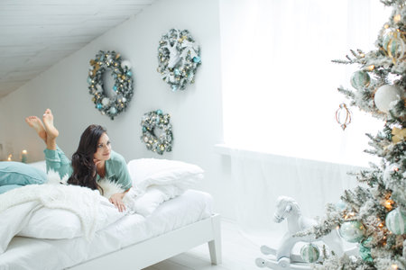 Woman in sweater, warm and cozy day in Christmas interior design, Christmas tree decorated with lights toys gifts, candles, lanterns, garland lighting indoors. High quality photo.の写真素材