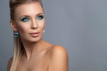 Hairstyle of a blonde high ponytail. Beauty Fashion Woman Portrait. Beautiful girl model with makeup, earrings and a ring, posing, isolated on studio background. High quality photo.の写真素材