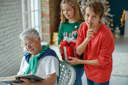 Grandfather and grandchildren in a room decorated for Christmas against the background of a Christmas tree. Christmas holiday concept. contrast photography. High quality photo.の写真素材