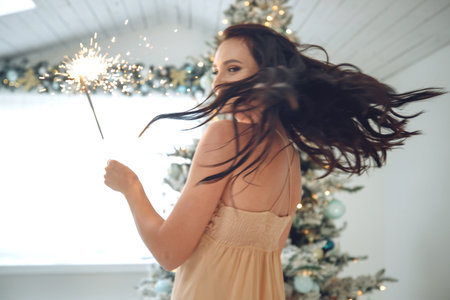 Beautiful girl brunette model posing with sparklers. Warm Christmas decor with fir tree. High quality photo.の写真素材