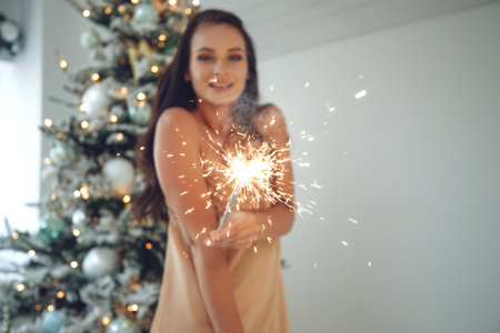 Beautiful girl brunette model posing with sparklers. Warm Christmas decor with fir tree. High quality photo.の写真素材