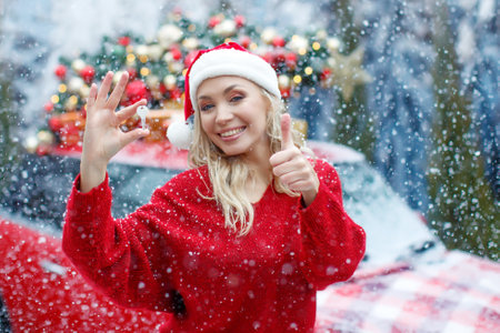 Beautiful young gorgeous woman close-up taking a photo key and smiling, a gift for Christmas, close-up photo, a girl received a key from a car, a red car. High quality photo.の写真素材