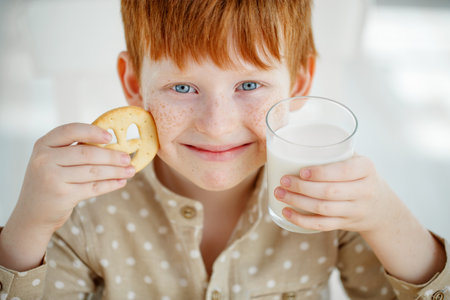 The child is having breakfast. The kid drinks milk and eats cookies. Children eat on a sunny morning. Healthy balanced nutrition for young children. High quality photo.の写真素材